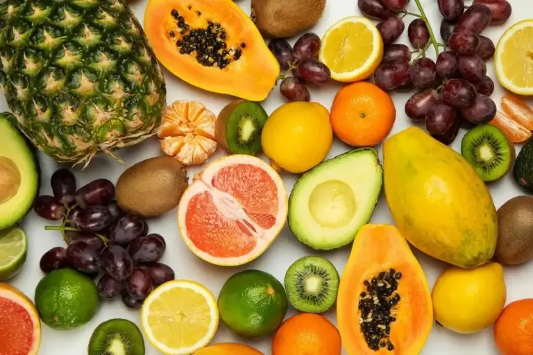 Assorted fresh fruit including papaya, citrus, kiwi, avocado, grapes and pineapple on a white surface